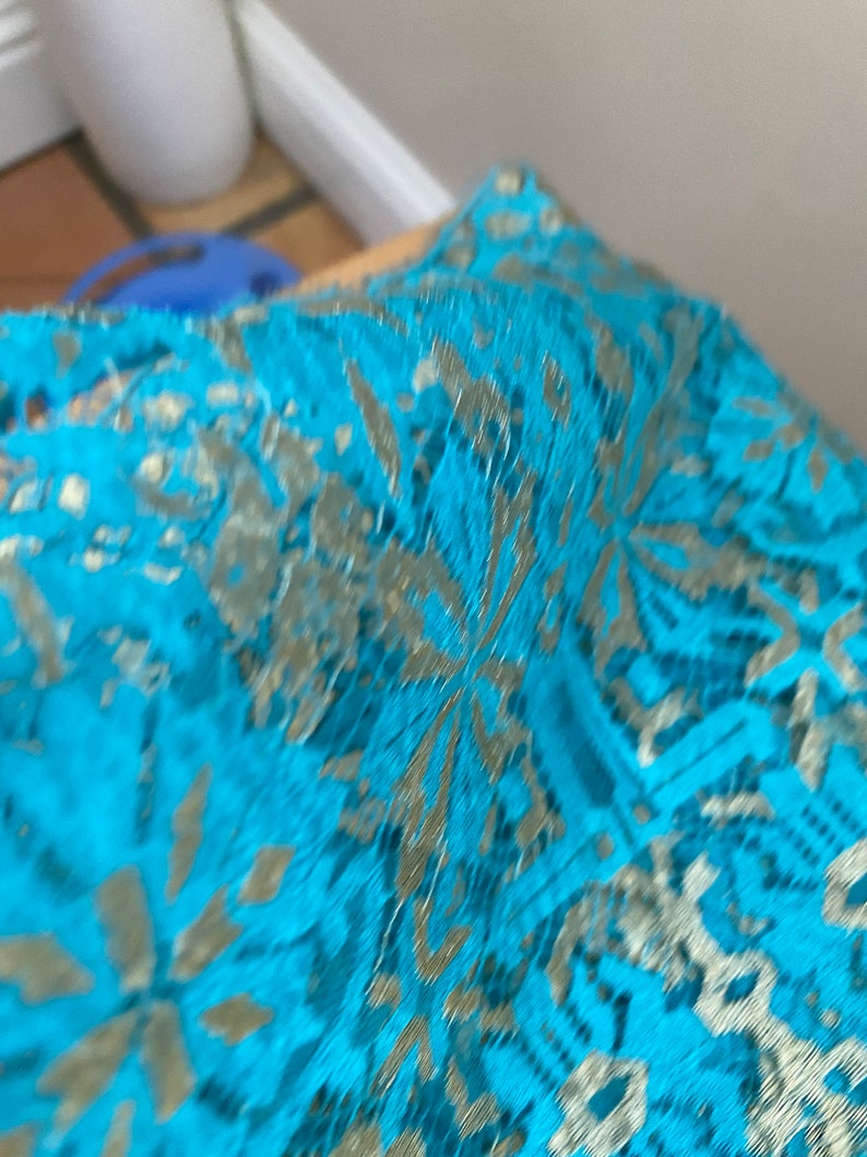 May include: Turquoise blue lace fabric with a gold metallic pattern. The lace has a delicate floral design.