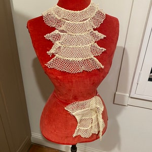 May include: A red fabric dress form with a white crocheted lace collar and a white crocheted lace sash.