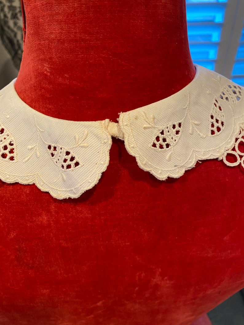 Puede incluir: Un cuello de encaje blanco con borde festoneado. El cuello est&aacute; sobre un maniqu&iacute; de terciopelo rojo.