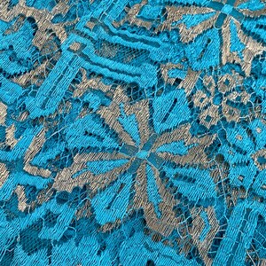 May include: Close-up of a turquoise lace fabric with a silver metallic pattern. The lace has a delicate floral design.