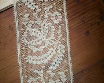 May include: A close-up of a white lace trim with a floral pattern. The lace is delicate and intricate, with a fine mesh design.
