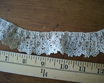 May include: A close-up of a white lace trim with a floral pattern. The lace is measured against a ruler, showing it is approximately 4 inches long.