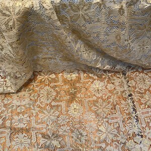May include: A close-up of a gold lace fabric with a delicate floral pattern. The fabric is soft and sheer, and it has a subtle shimmer.