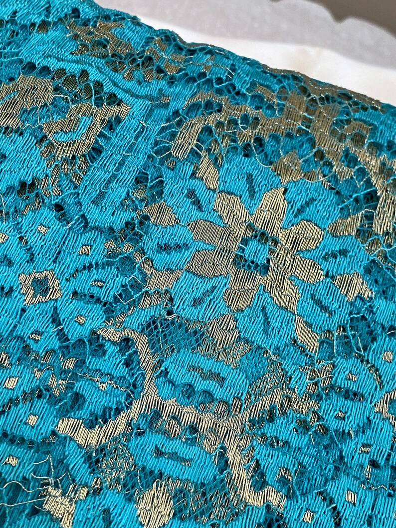 May include: Teal lace fabric with a silver floral pattern.