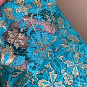 May include: Teal lace fabric with a gold metallic pattern. The lace has a delicate floral design.