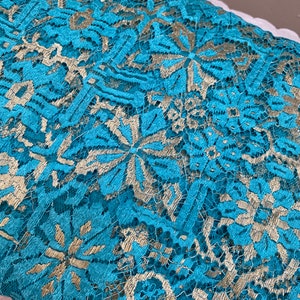 May include: Teal lace fabric with a gold metallic pattern. The lace has a delicate floral design.