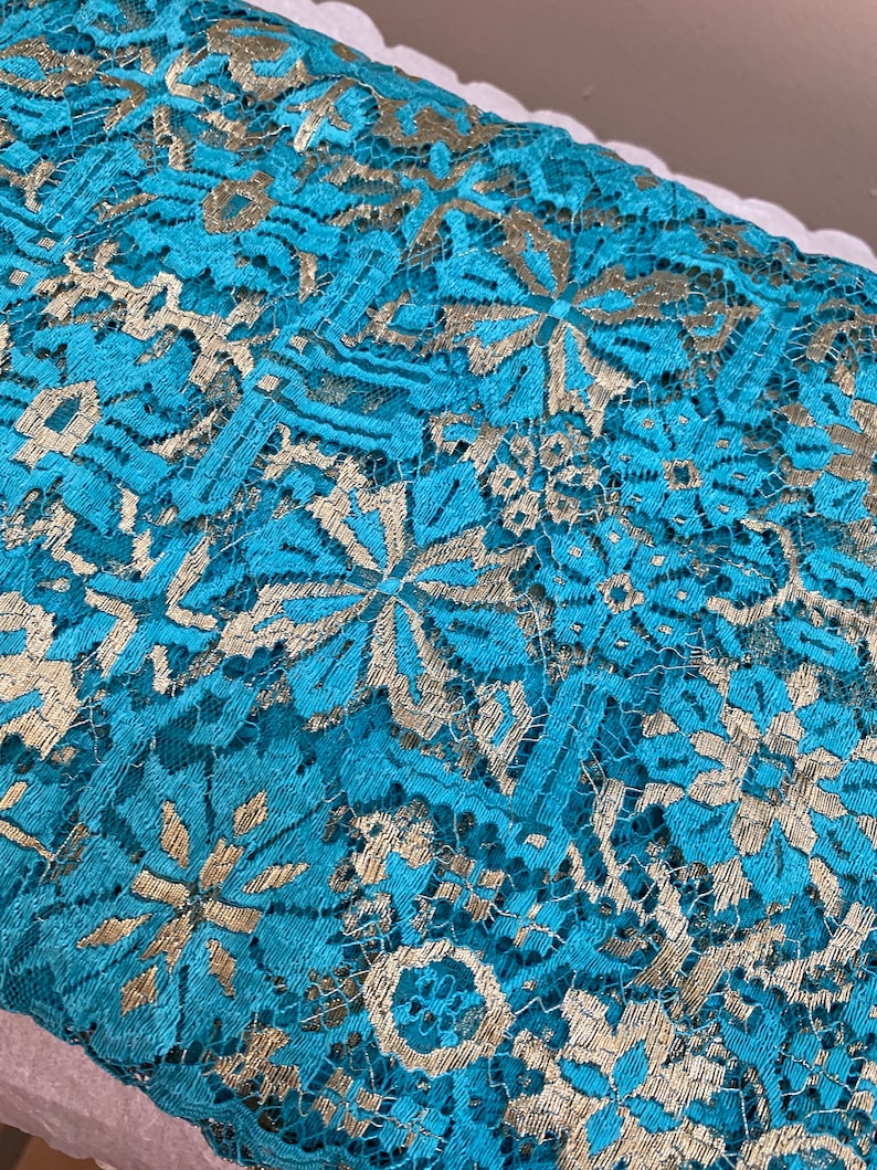 May include: Teal lace fabric with a gold metallic pattern. The lace has a delicate floral design.