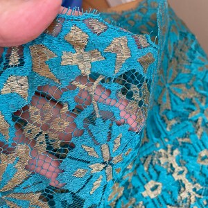 May include: Teal lace fabric with gold embroidery. The lace has a floral pattern.