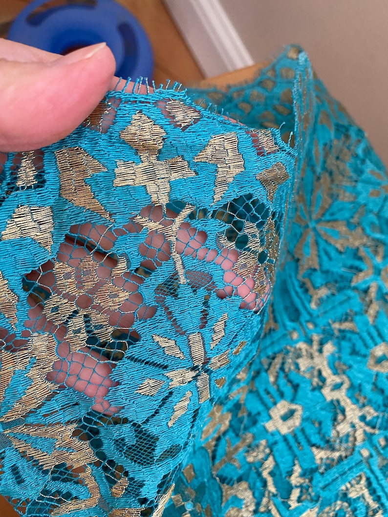 May include: Teal lace fabric with gold embroidery. The lace has a floral pattern.