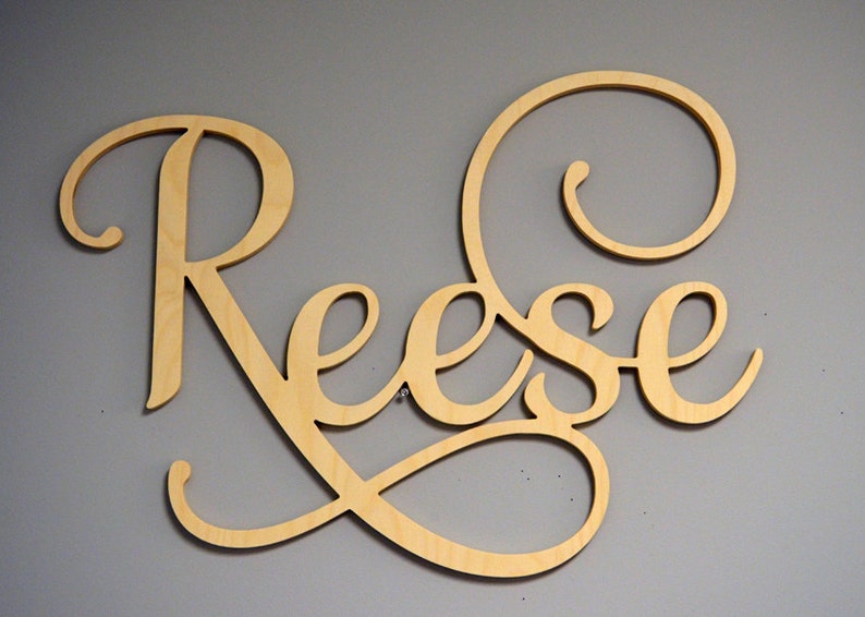 Może przedstawiać: Drewniany znak z napisem "Reese" napisanym kursywą. Znak jest pomalowany na jasny kolor drewna i ma ozdobny zw&oacute;j na końcu nazwy.
