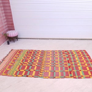 May include: A red, yellow, and green woven rug with a checkered pattern. The rug is laid out on a white tiled floor.