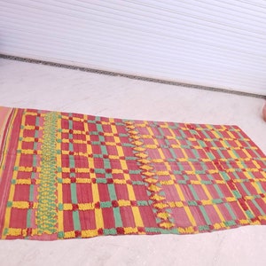 May include: A rectangular woven rug with a checkered pattern in shades of red, yellow, and green. The rug has a fringe border and a textured surface.