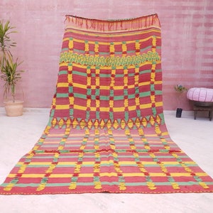 May include: A colorful Moroccan rug with a geometric pattern in shades of red, green, and yellow. The rug has a woven texture and is made of wool.