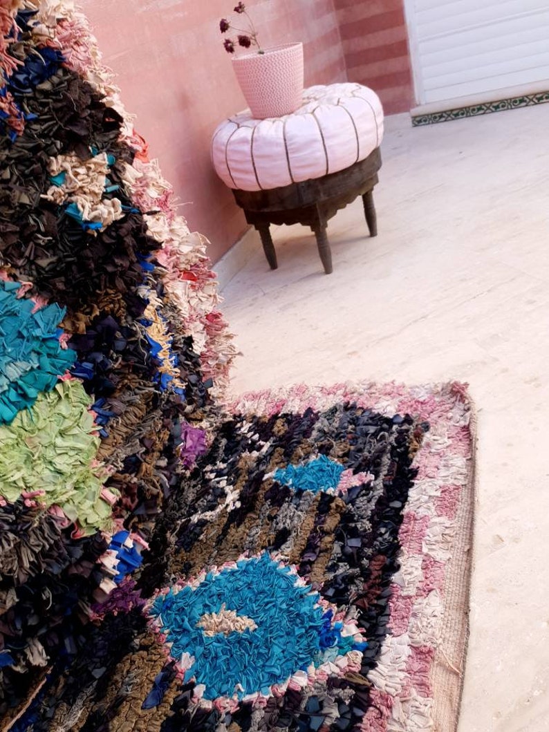 Puede incluir: Primer plano de una alfombra colorida tejida a mano con un patr&oacute;n azul, rosa y blanco. La alfombra est&aacute; hecha de materiales reciclados y tiene un aspecto texturizado &uacute;nico.