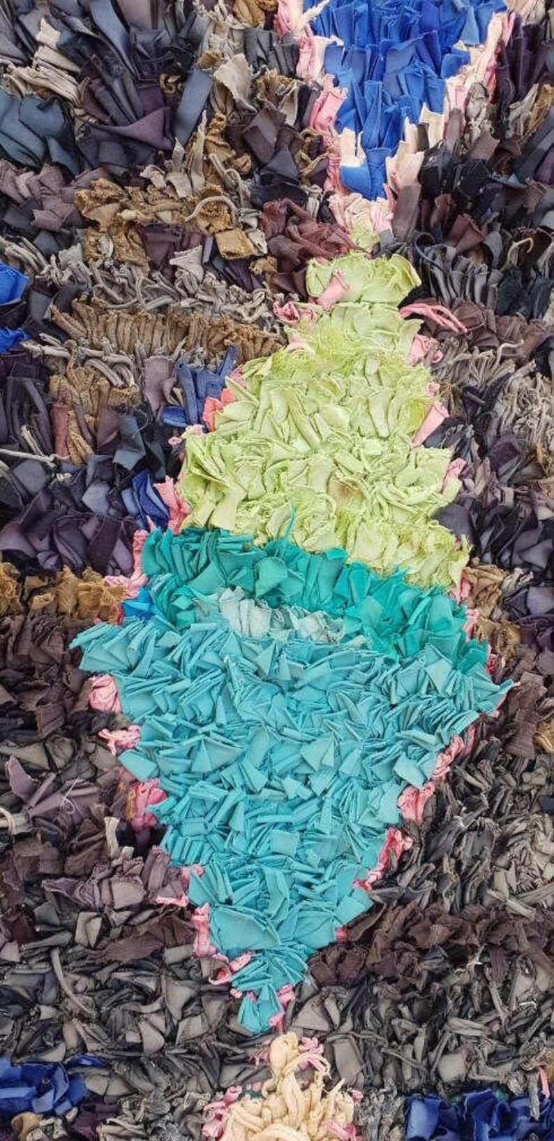 Puede incluir: Una alfombra colorida hecha de recortes de tela reciclados. La alfombra presenta una forma de diamante en tonos de verde, azul y rosa.