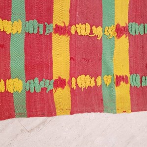 May include: A woven rug with red, yellow, and green stripes. The rug has a textured surface with raised loops in yellow and green.