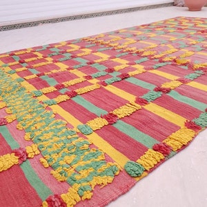 May include: A colorful striped rug with a textured woven design in shades of pink, yellow, and green. The rug has a geometric pattern with a fringe border.