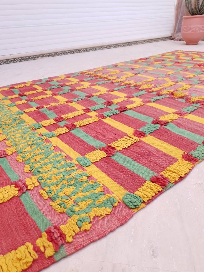 May include: A colorful striped rug with a textured woven design in shades of pink, yellow, and green. The rug has a geometric pattern with a fringe border.