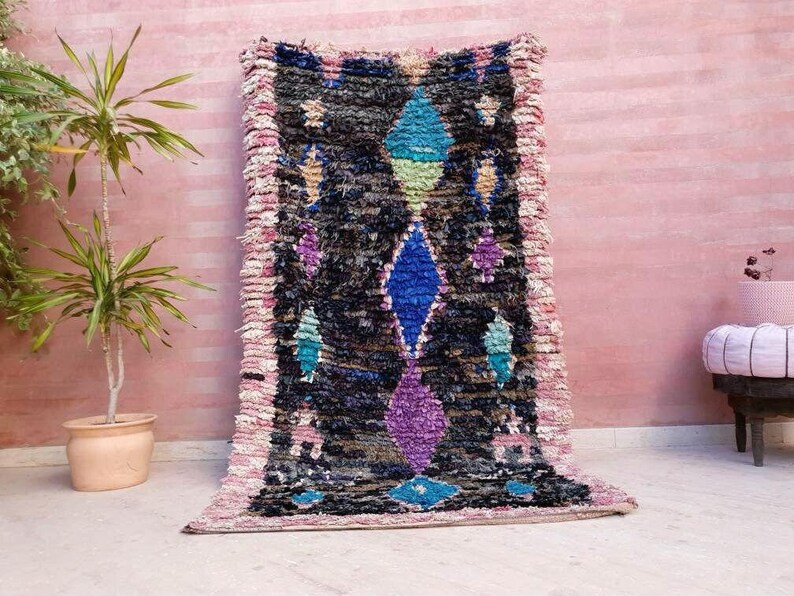 Puede incluir: Una alfombra marroqu&iacute; colorida con un patr&oacute;n geom&eacute;trico en tonos de azul, rosa, morado y verde. La alfombra tiene un borde con flecos y est&aacute; hecha de lana.