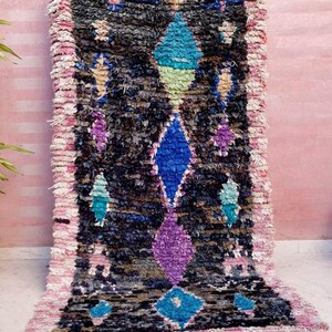 Puede incluir: Una alfombra marroqu&iacute; colorida con un patr&oacute;n geom&eacute;trico en tonos de azul, verde, morado y rosa. La alfombra tiene un aspecto desgastado y vintage y est&aacute; hecha de lana.