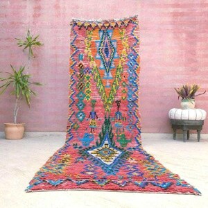 May include: A vibrant, hand-woven rug with a geometric design. The rug features a mix of colors, including pink, blue, orange, and green. The rug is rectangular and appears to be made of wool or a similar material.