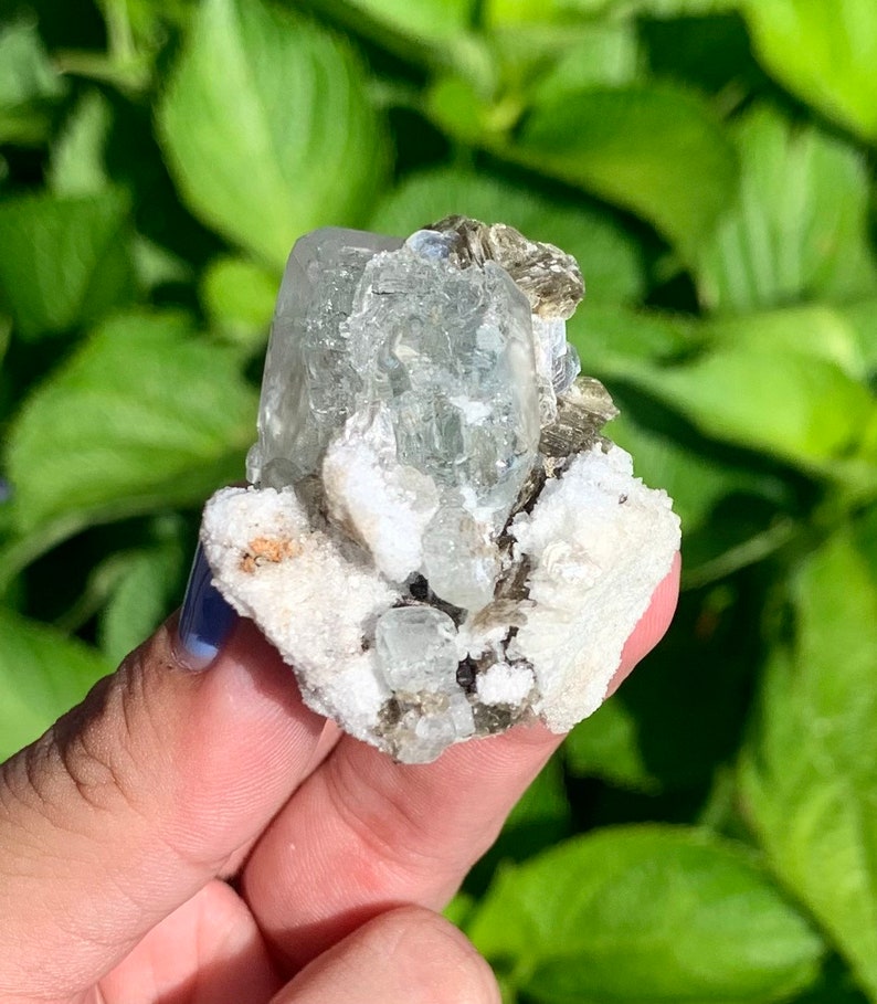Puede incluir: Un c&uacute;mulo de cristales de aguamarina verde con una matriz blanca y gris. Los cristales son transparentes y tienen un ligero tono verde. La matriz es rugosa y texturizada.