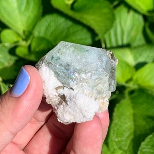 Puede incluir: Un cristal de aguamarina azul claro con una matriz blanca. El cristal est&aacute; facetado y tiene un ligero brillo iridiscente.
