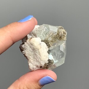 Puede incluir: Un grupo de cristales de aguamarina verde claro con una matriz blanca. Los cristales son transl&uacute;cidos y tienen un ligero brillo. Los cristales de aguamarina est&aacute;n rodeados por una matriz blanca.