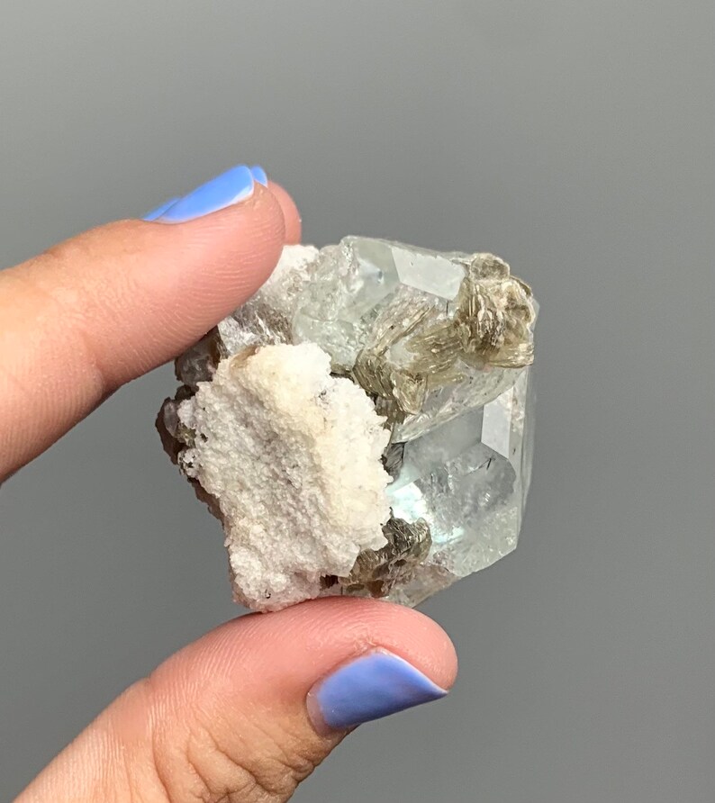 Puede incluir: Un grupo de cristales de aguamarina verde claro con una matriz blanca. Los cristales son transl&uacute;cidos y tienen un ligero brillo. Los cristales de aguamarina est&aacute;n rodeados por una matriz blanca.