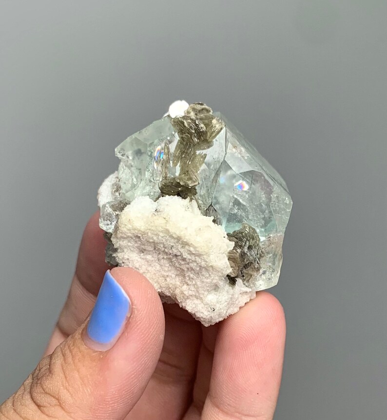 Puede incluir: Un grupo de cristales de fluorita verde claro con una matriz blanca. Los cristales de fluorita son transl&uacute;cidos y tienen un brillo v&iacute;treo. La matriz est&aacute; cubierta de peque&ntilde;os cristales grises.