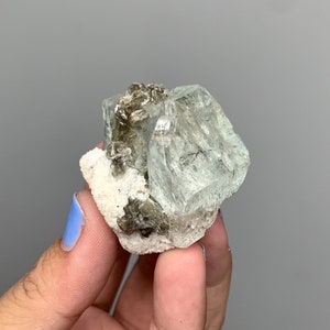 Puede incluir: Un grupo de cristales de aguamarina verde claro con una matriz blanca. Los cristales son transl&uacute;cidos y tienen un brillo v&iacute;treo.