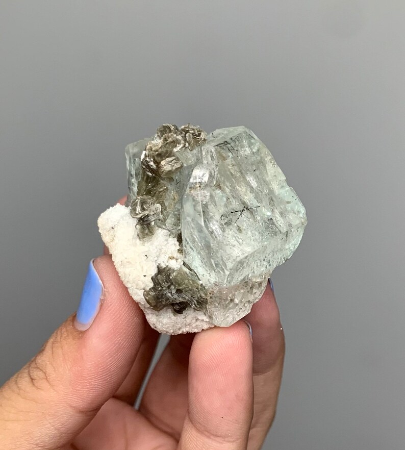 Puede incluir: Un grupo de cristales de aguamarina verde claro con una matriz blanca. Los cristales son transl&uacute;cidos y tienen un brillo v&iacute;treo.