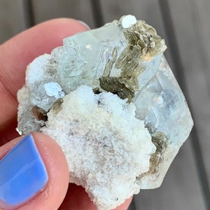 Puede incluir: Un c&uacute;mulo de cristales de aguamarina transparentes y facetados con inclusiones verdes, engastado en una matriz blanca. El cristal mide aproximadamente 5 cm.