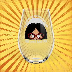 May include: A stemless wine glass with a cartoon image of a woman wearing red glasses. The glass has the text "My Momma Doesn't Get Drunk, She Just Has Fun" in white lettering. The background is yellow with orange rays.