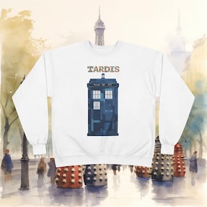 Peut inclure: Sweat-shirt blanc avec un motif bleu de TARDIS et le mot "TARDIS" au-dessus en lettres colorées. Le design est inspiré de la série télévisée britannique de science-fiction Doctor Who. L'arrière-plan montre une peinture à l'aquarelle d'une scène de ville.