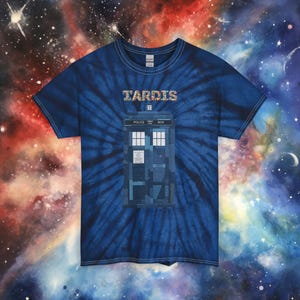 Puede incluir: Camiseta azul teñida con un diseño de la cabina telefónica TARDIS de Doctor Who. La palabra "TARDIS" está impresa en letras coloridas. La camiseta tiene cuello redondo y mangas cortas.