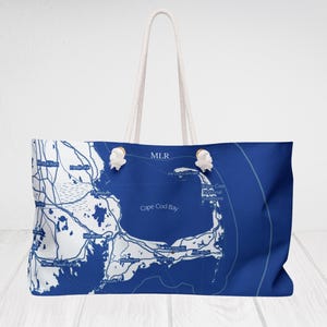 May include: A large blue tote bag with a white map design of Cape Cod. The bag has white rope handles and decorative white knots. The text "MLR" is printed on the bag.