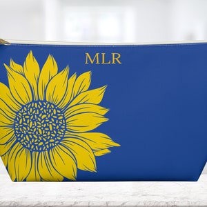 May include: A blue zippered pouch with a yellow sunflower design and the initials "MLR" in gold.