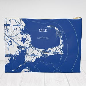 Peut inclure: Une pochette zippée bleue et blanche représentant une carte détaillée de la baie de Cape Cod, avec le texte "MLR" et des noms de lieux. La pochette a une fermeture éclair dorée et est probablement en tissu.