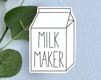 May include: A white sticker shaped like a milk carton with a black outline and the text MILK MAKER printed in black capital letters on the front. The sticker is positioned next to a green eucalyptus branch with several rounded leaves.