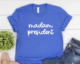 May include: A royal blue t-shirt with the text "madam president" in white cursive lettering.