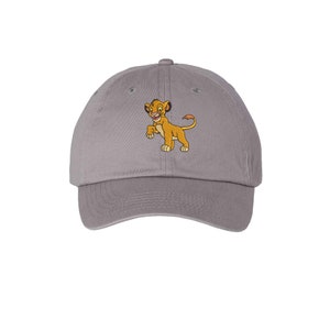 May include: A grey baseball cap featuring an embroidered graphic of a small, golden-brown lion cub standing on its hind legs. The cap has a curved brim, a button on top, and stitched eyelets for ventilation, providing a classic structured look.