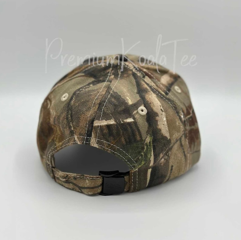 May include: A baseball cap featuring a brown, green, and tan camouflage pattern. The cap has a black plastic adjustable strap closure at the back and light-colored eyelets on the crown. The text PremiumKoalaTee is visible in the background.