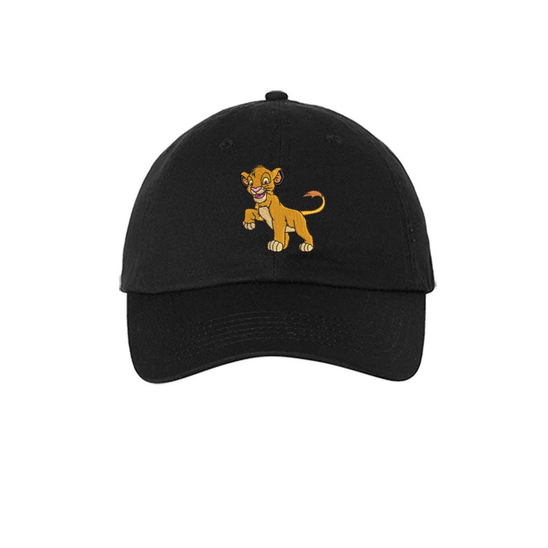 May include: A black baseball cap featuring an embroidered graphic of a young lion character with golden-brown fur, a light tan underbelly, and a tufted tail. The cap has a curved brim, a button on the top, and stitched eyelets for ventilation.