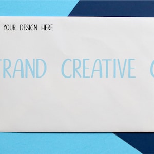 May include: A white envelope with the text "YOUR DESIGN HERE" at the top and "STRAND CREATIVE CO" at the bottom. The envelope is on a blue and dark blue background.