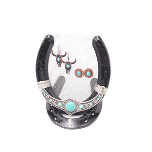 May include: A black horseshoe with a wire mesh center, decorated with turquoise and silver accents, used as a jewelry stand.  The stand is displaying a pair of turquoise and silver earrings and a pair of turquoise and copper earrings.