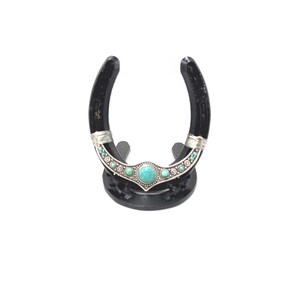 May include: Black horseshoe with a turquoise and silver design, mounted on a black stand.