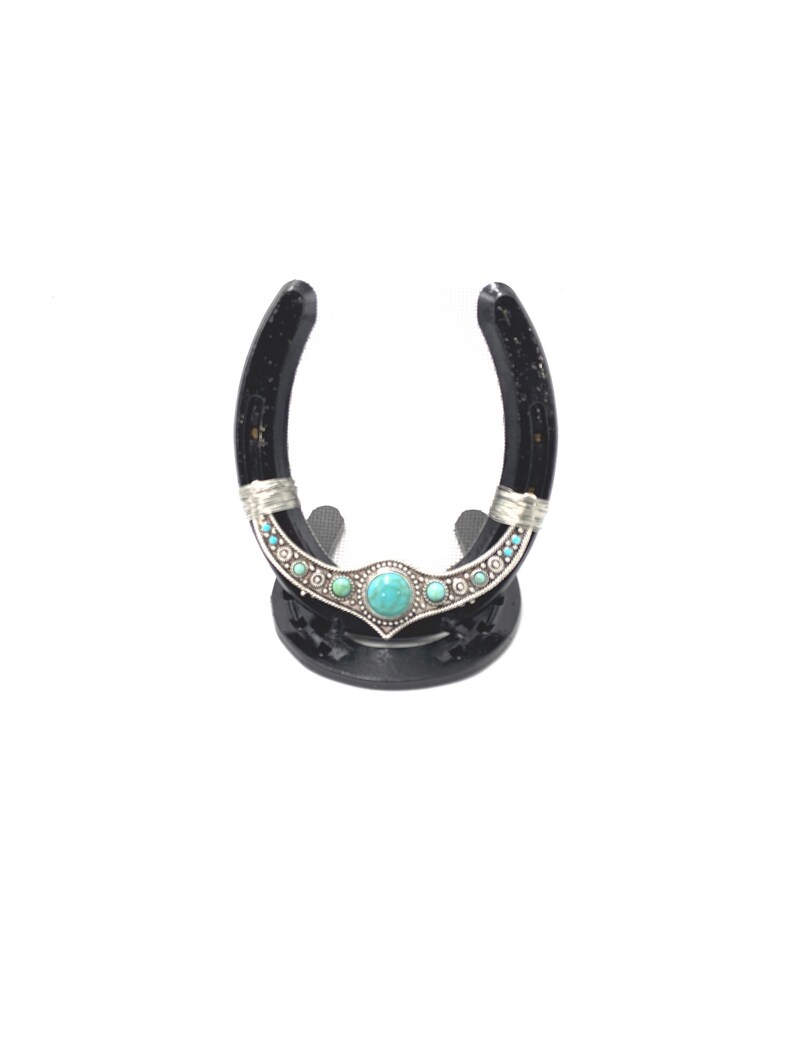 May include: Black horseshoe with a turquoise and silver design, mounted on a black stand.