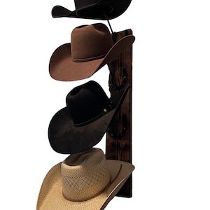 May include: A wooden hat rack with four cowboy hats hanging on it. The hats are brown, black, and straw.