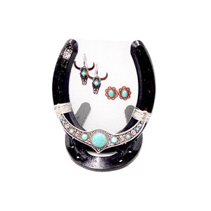 May include: A black horseshoe-shaped jewelry stand with turquoise and silver accents. The stand is decorated with a turquoise and silver design and features a mesh backing. The stand is displaying a pair of turquoise and silver earrings and a pair of turquoise and silver stud earrings.